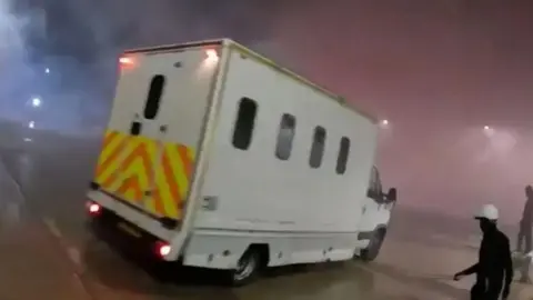 The Palestinian Screenshot action of the video is uploaded by the Palestine action. It shows a white van with a curved curvature of a taller and vers to yellow and citrus in the back. Time at night and there are many smoke in the air that is lit by red brake lights. On the right hand is a figure wearing all black and white hat.