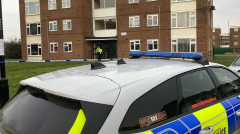 A block of flats in South Yorkshire with a police officer standing outside and a police car at the front of the image