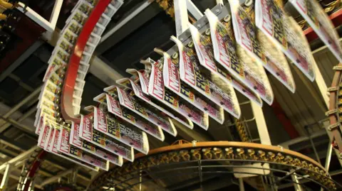 Getty Images An extensive network of overhead conveyor tracks winds through the Watford printing plant, carrying freshly printed newspapers. "Daily Mirror" appears at the top of many copies.