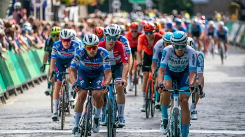 PA Media The peloton passes through the town centre on stage one of the 2024 Lloyds Bank Tour of Britain Men in Kelso in the Scottish Borders.