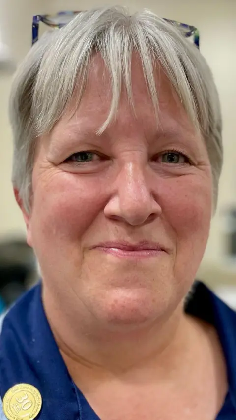 Close up of blonde woman smiling wearing a blue NHS uniform