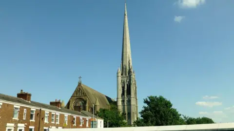 RudeHealth/Geograph A street view of Church of St. Walburge, Preston on a sunny day close to a row of terraced homes. 