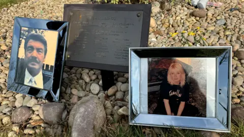 A memorial to Jane Roche's dad and sister. There are two picture frames showing a man with dark hair and a thick dark moustache and another photo frame showing a woman with short blonde hair wearing a black T-shirt.