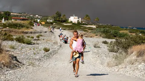 Getty Images Tourists are evacuated as huge wildfire rages across Greece