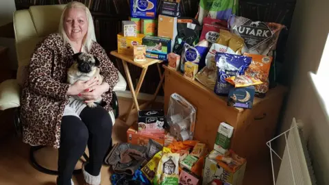 Helping Hands Animal Foodbank Charlotte Harris holding a dog and surrounded by pet food