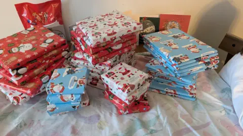 Kirsty A pile of presents on a table in different coloured wrapping paper. There are blue, white and red patterned Christmas presents.