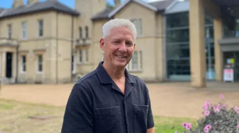 A man in a dark coloured shirt standing in front of a large museum which is blurry in the background