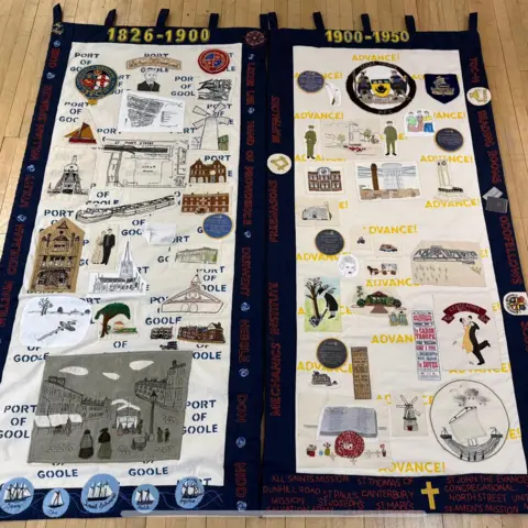 The photo shows two pieces of fabric laid on the floor. They are both covered with various different images that have been embroidered.