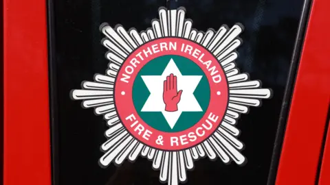 The NI fire service logo on the side of a red fire appliance 