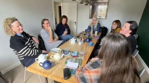 Shaun Whitmore/BBC People gathered around a table
