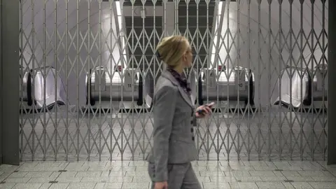 Getty Images Woman walks past gated station