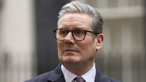 PA Media Sir Keir Starmer is looking away from the camera. He has short grey hair and is wearing glasses. He is wearing a white shirt and tie and suit jacket. 