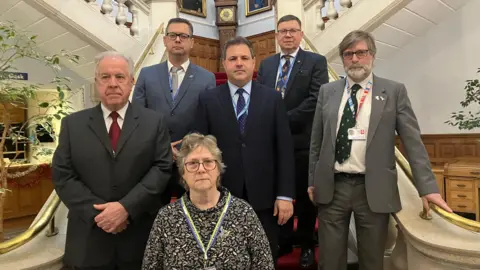 SIMON FINLAY/LDRS Six people, five men and a woman, pose on the large staircase inside County Hall in Maidstone, all looking directly into the camera.