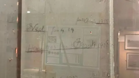 Pencil height markings and names are written on a door which is covered in a transparent plastic case.