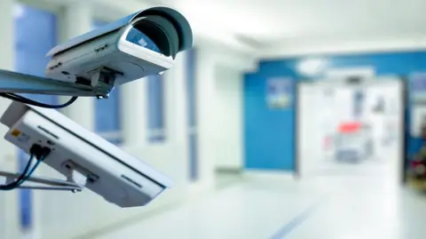 A close up of security cameras in an empty hospital corridor.  The corridor is blurred out in this stock image. 