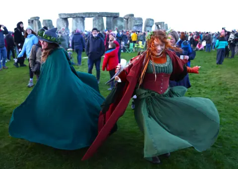 EPA Revelers dance near Stonehenge wearing green and red dresses and capes.