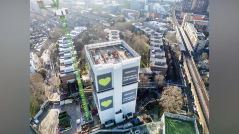Getty Images An aerial view of Grenfell Tower in the process of deconstruction. It is wrapped in a cover and is surrounded by low rise housing. 