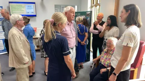 Volunteers, patients, nurses and doctors chat in the reception area of the surgery.