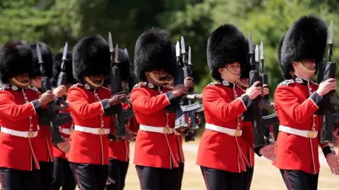 Reuters Members of the Scots Guards, men dressed in red tunics and black bearskin caps, march while holding ceremonial black rifles to their shoulders.
