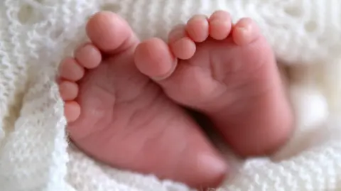 A newborn baby's feet poking out of a white knitted blanket.