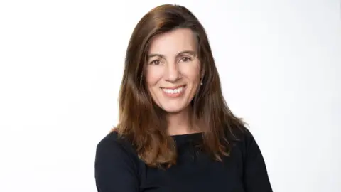 Jennifer Evans Photo of Tanya Tracey, CEO of Girls are Investors. She has long brown hair, is wearing a black long sleeved top and is smiling at the camera.