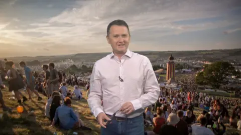 Matt standing in front of a picture of people on Glastonbury field