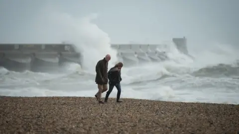 LEON NEAL View of two people braced against the wind on the beach at Brighton marina, East Sussex