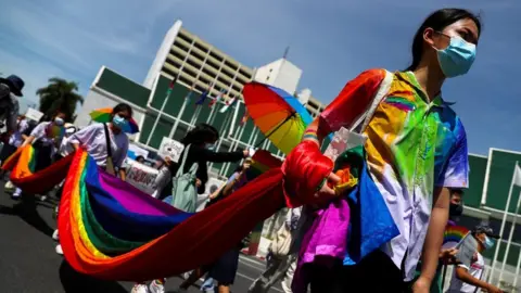 Members of a youth pride student group carry a long piece of rainbow-patterned fabric