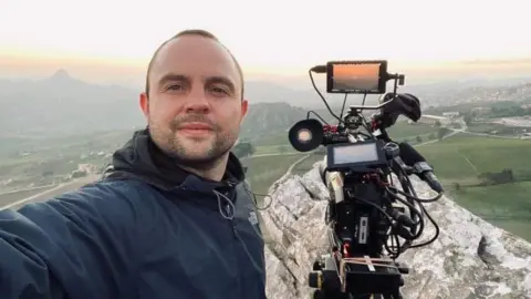 Kenny Fillingham Kenny Fillingham with camera, view of mountain landscape behind