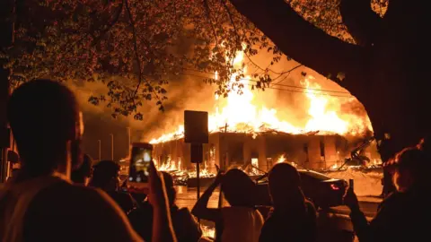 Getty Images People look on as a construction site burns in a large fire near the Third Police Precinct