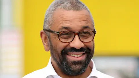 Reuters Headshot of a smiling James Cleverly, wearing a white shirt and tortoiseshell glasses 