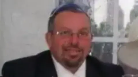 Facebook A pixelated photo of Melvin Cravits smiling at the camera. He wears glasses and has a moustache and a trimmed beard.