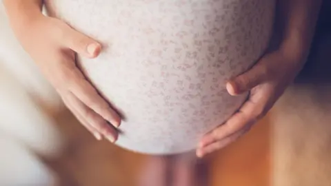 Looking down on a woman's heavily pregnant tummy, with both hands on either side of it 