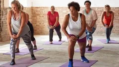 A group of six women in a room stretching. 