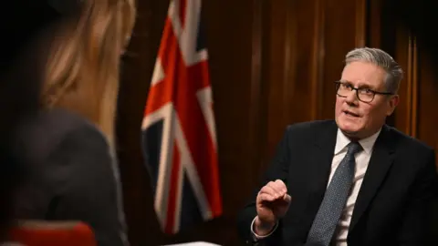 Jeff Overs/BBC/PA Wire Prime Minister Sir Keir Starmer being interviewed by Laura Kuenssberg for the BBC's Sunday with Laura Kuenssberg programme. He wears a black suit, a white shirt and a navy patterned tie. 