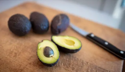 A sliced avocado on a chopping board next to a knife