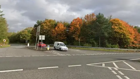Google the crossing of the A69 with the B6318. A white mini of and a red car are waiting in B6318 Junction to climb to the A69. There is a sign of national and white speed limit at the crossroads.