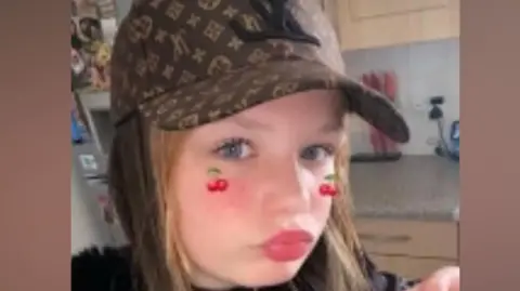 A girl wearing a baseball cap and posing for the camera in a selfie-style image.