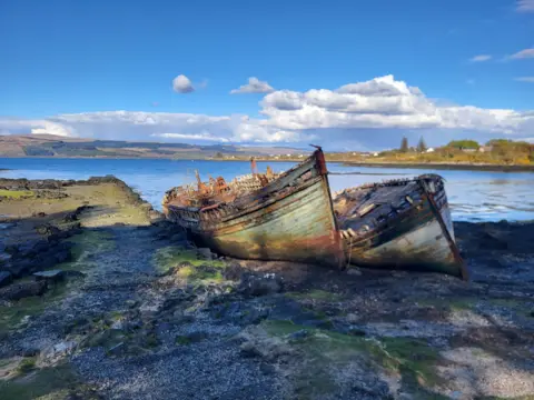 Ben Goodlad Two hulls of rusting boats near the shoreline