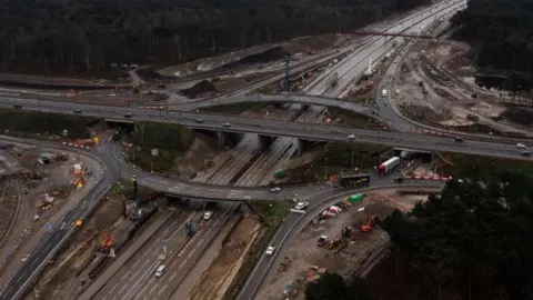 An aerial view of a motorway junction which includes a raised roundabout.