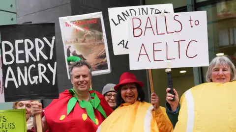 PA Media Protesters outside the Rolls Building of the Royal Courts of Justice, in central London. They are holding signs which say "Berry angry" and "Balls to AELTC". Two are dressed as yellow tennis balls while another as a strawberry.