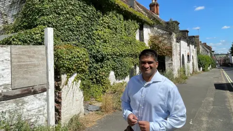 West Suffolk Council A man wearing a blue shirt standing in front of a derelict building with green leaves growing out of it in Newmarket.