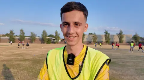Arvin, 18, recently arrived in Oxford from Iran. He is wearing a yellow bib over an Oxford United shirt, and has short dark hair. he looks young.