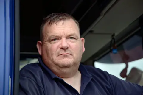 A close up picture of Mr Barnes in his lorry cab. His expression is serious but friendly