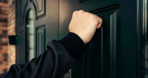 Getty Images A hand knocking on a black door
