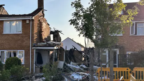 A house in Yate where a suspected gas explosion happened. The roof of the property is gone and there is damage to the side of the building. Debris can be seen all over the ground by the front door.
