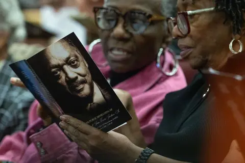Getty Images Two women are seen looking through a booklet for the funeral service with the cover showing the face of the civil rights leader.