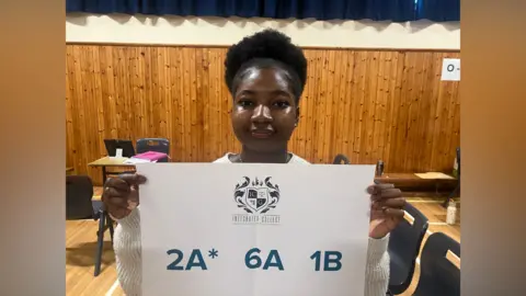 Girl with hair tied up holding sign with her results two A stars, 6six As and one B
