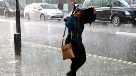 Woman walking in heavy rain holding a jacket over her head.