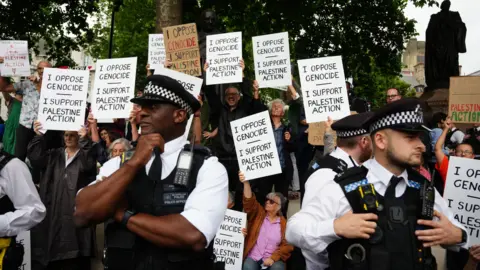 PA Media People holding signs and placards in support of Palestine Action, surrounded by police